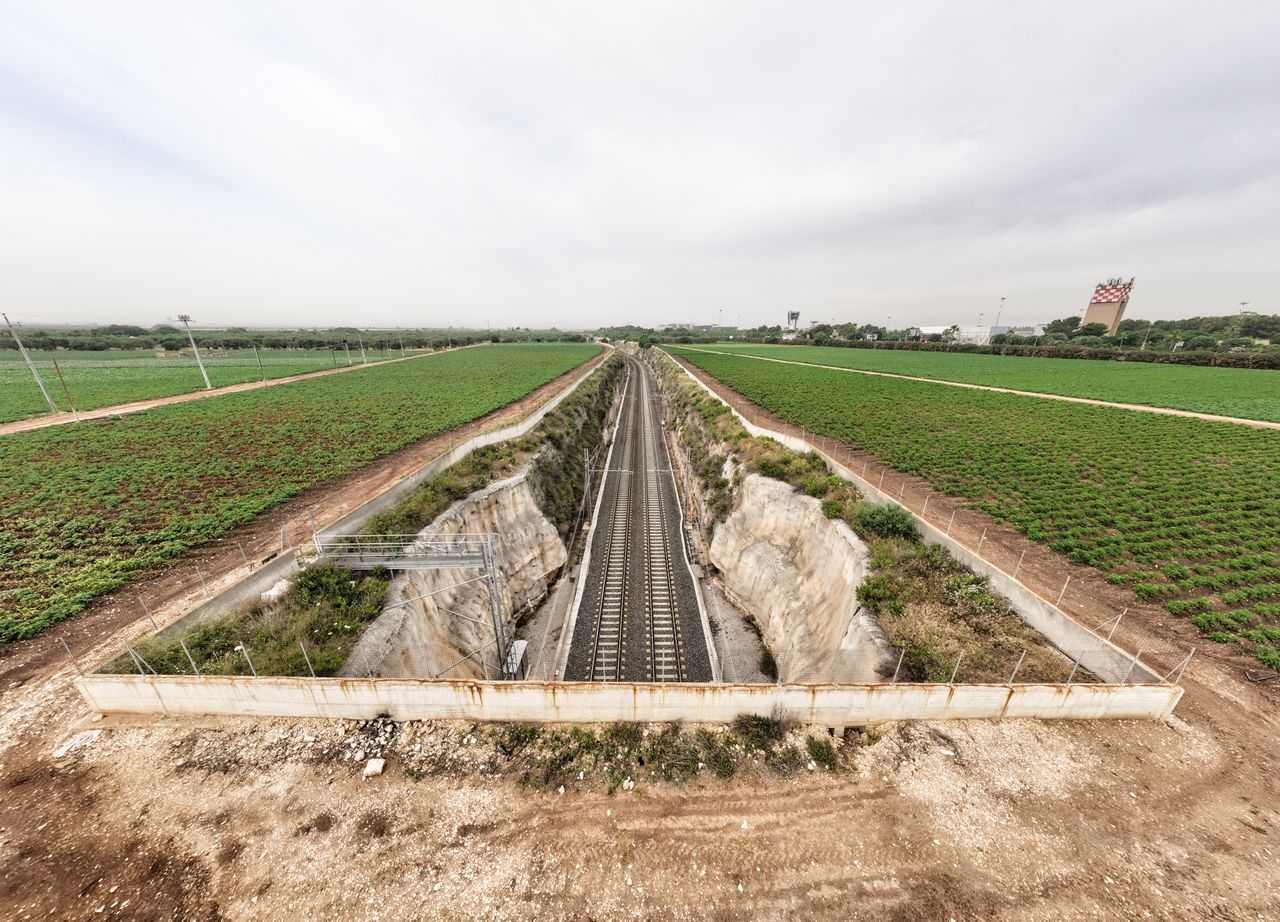 Aerial view of railway cutting through vibrant green fields in rural countryside.