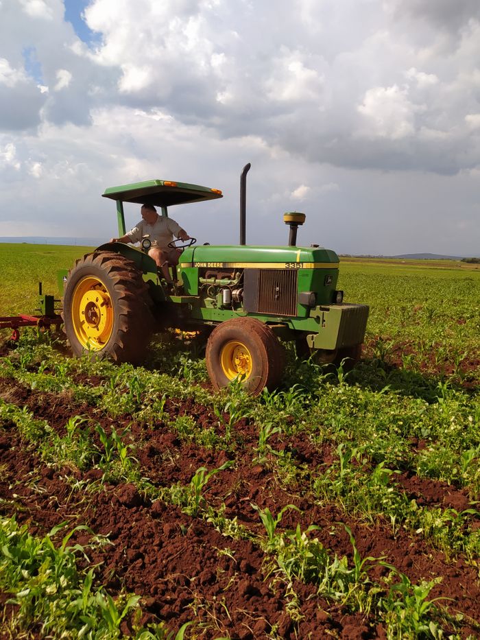 A farmer operating a tractor in a lush green field, demonstrating agricultural work under a cloudy sky.