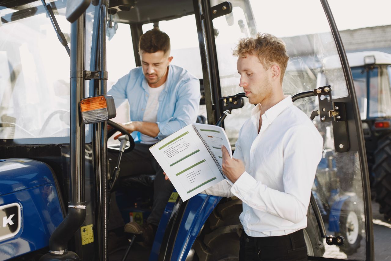 Two men reviewing documents near farm machinery, highlighting agricultural operation.